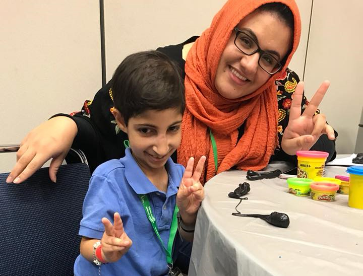 MUHSEN's convention services coordinator and a boy with special needs are throwing up peace signs.