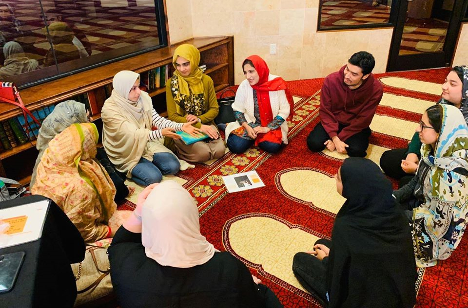 9 women and 1 men are sitting in a circle and participating in a professionally-led MUHSEN support group hosted at the masjid.