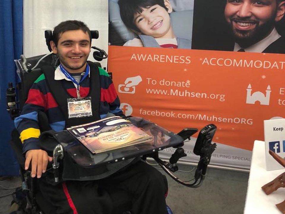 A young man in a wheelchair posing in front of the MUHSEN banner.