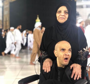 A single mom standing behind her son in a wheelchair during MUHSEN Umrah.