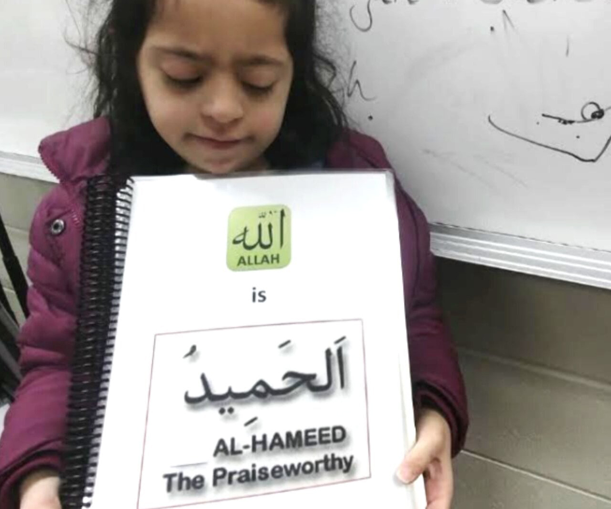 young girl holding a workbook that says "Allah is Al-Hameed, the praiseworthy"